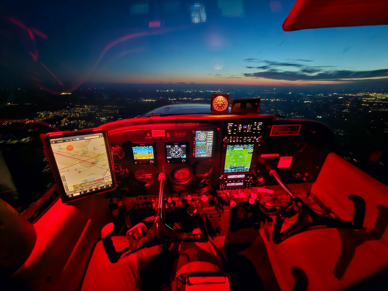 Cessna 172H cockpit at dusk with red instrument lighting over the lights of a Texas city